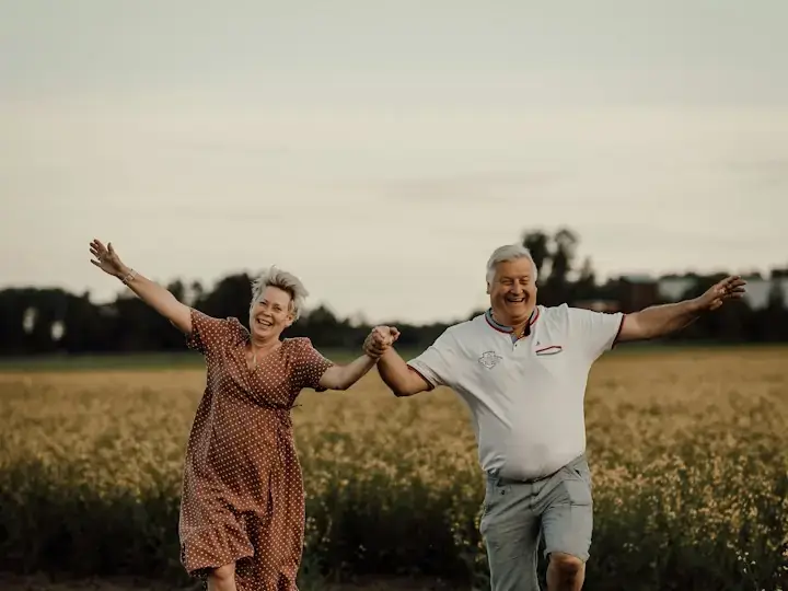 Fröhliches älteres Paar läuft Hand in Hand über ein Feld