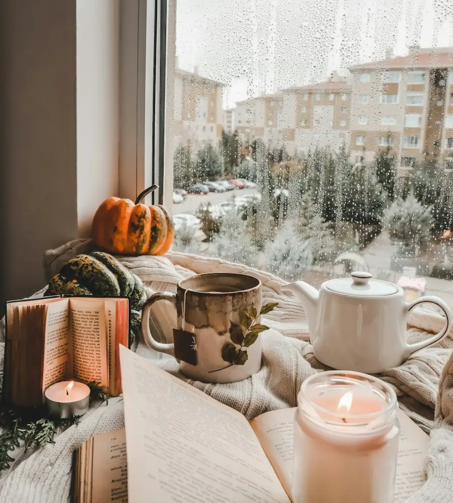 Tee, Kerze und Buch am Fenster an einem regnerischen Herbsttag